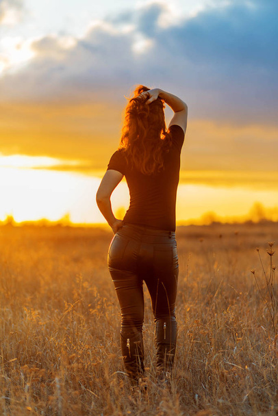 Nő nadrágban és pólóban, pózol a naplemente hátterében, visszapillantva. A természet szépsége. - Fotó, kép
