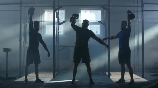 Slow motion: group fitness training of athletes in an atmospheric fitness room against the background of sunlight rays synchronously lift up kettlebell - 映像、動画
