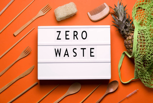 lightbox que diz zero resíduos ao lado de talheres feitos de madeira e um saco ecológico em um fundo laranja
 - Foto, Imagem