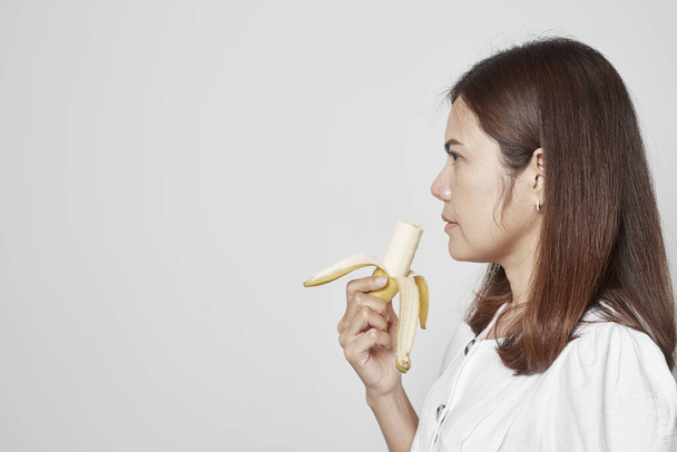 Молодая азиатка держит банановый желтый сырой. концепция правильного питания. уход за телом, на сером фоне
 - Фото, изображение