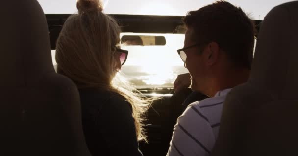 Rear view of a happy Caucasian couple enjoying free time during road trip together, sitting inside an open top car, driving and smiling with blue sky and sea in the background in slow motion - 映像、動画