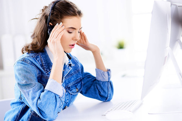 Moe vrouwelijke klantenserviceoperator in het kantoor met headset - Foto, afbeelding