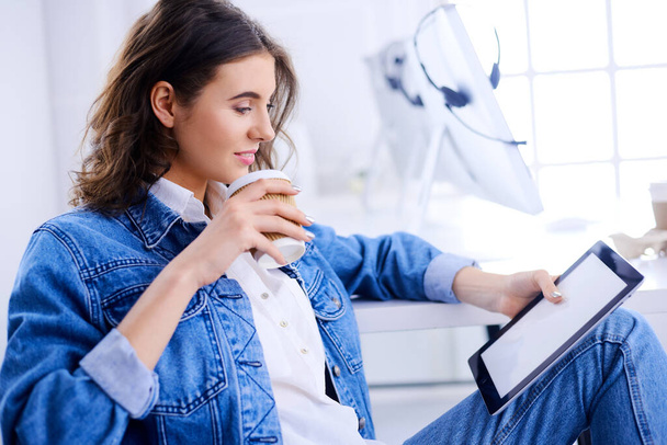 Μια κοπέλα δουλεύει στο γραφείο με ένα τάμπλετ. Μαθητής πίνει καφέ στη σοφίτα. - Φωτογραφία, εικόνα