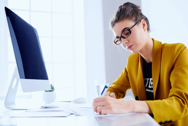 Portret van zakenvrouw met desktop schrijft op een document op haar kantoor - Foto, afbeelding