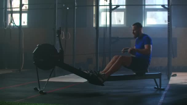 Slow motion: one man in an atmospheric fitness room in the sunlight in a rowing machine. Rower trains, cardio athlete training - Footage, Video