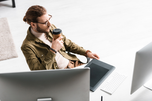 Duży kąt widzenia cyfrowego projektanta picia kawy w pobliżu komputerów i tabletów graficznych na stole - Zdjęcie, obraz