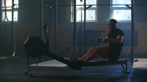 Slow motion: one man in an atmospheric fitness room in the sunlight in a rowing machine. Rower trains, cardio athlete training - Felvétel, videó