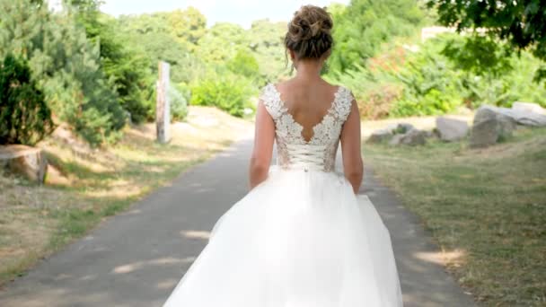 4k Zeitlupe Video von jungen schönen Braut in langen weißen Kleid zu Fuß weg auf dem Weg in den Park - Filmmaterial, Video