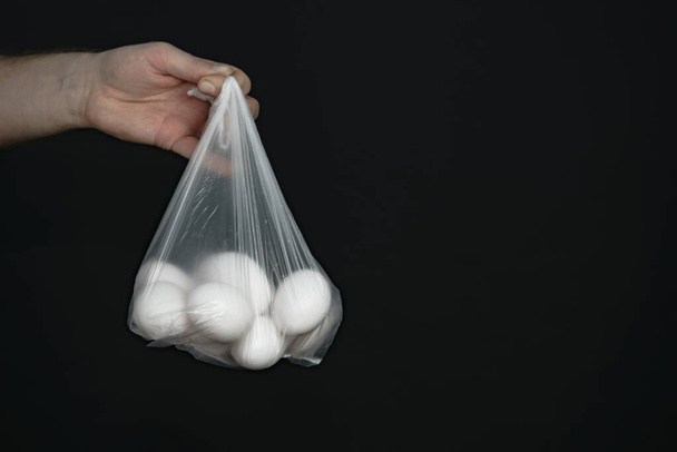 Hand holding plastic bag with white eggs on a black background.   - Fotoğraf, Görsel