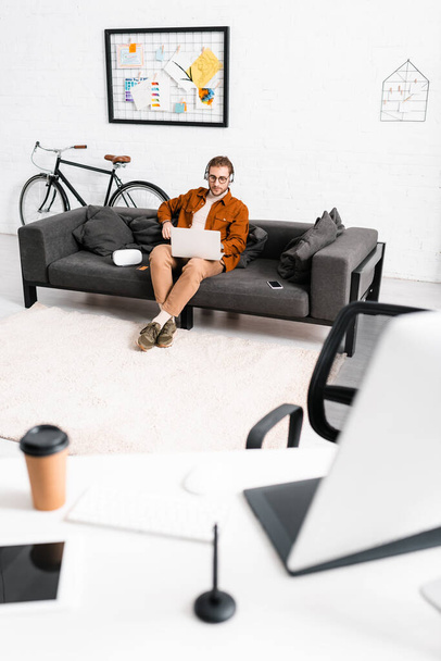Επιλεκτική εστίαση του 3D καλλιτέχνη στα ακουστικά χρησιμοποιώντας φορητό υπολογιστή κοντά στο smartphone και τα ακουστικά εικονικής πραγματικότητας στον καναπέ στο γραφείο  - Φωτογραφία, εικόνα