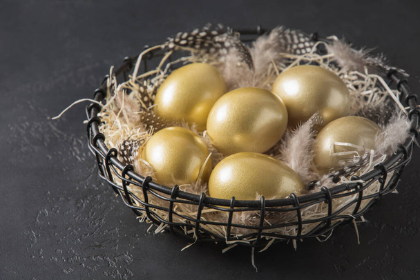 Chicken colored golden eggs in decorative vase on black background. Easter dark concept. Close up and copy space. - Photo, image