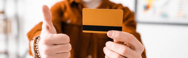 Vista cortada do artista 3d segurando cartão de crédito e empurrando o polegar para cima, tiro panorâmico
  - Foto, Imagem