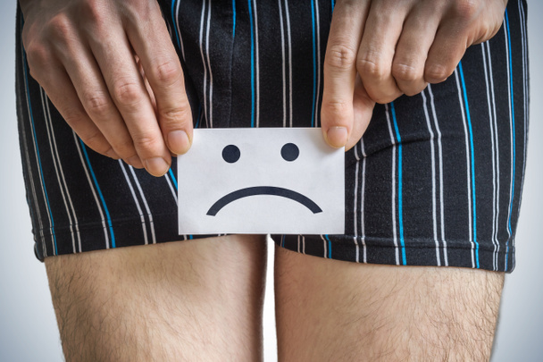Urinary or prostate problems concept. Young man holds paper with sad smiley. - Photo, Image
