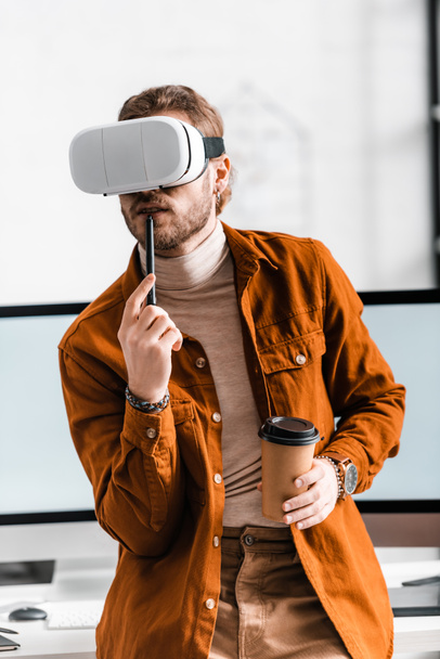 Digital designer in vr headset holding stylus of graphics tablet and coffee to go near computer monitors in office  - Foto, imagen