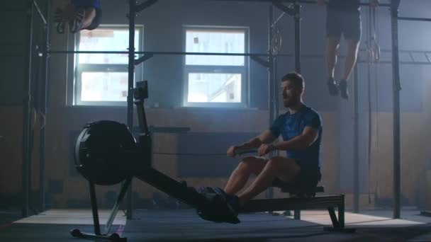 Slow-motion cross-training, three men in the fitness room, two pulling up in the background, one using a rowing machine. - Filmagem, Vídeo