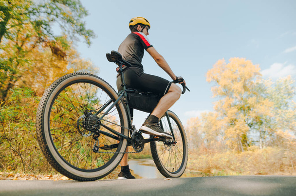 Κοντινή φωτογραφία ενός αθλητικού άνδρα που κάθεται σε ένα ποδήλατο και κοιτάζει το όμορφο φθινοπωρινό τοπίο. Ποδηλάτης σταμάτησε να χαλαρώσει και να θαυμάσει την φθινοπωρινή φύση. Ενεργό σχέδιο διακοπών. Ποδηλασία είναι ένα χόμπι - Φωτογραφία, εικόνα