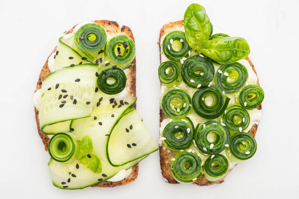top view of fresh cucumber toasts with seeds and basil leaves isolated on white - 写真・画像
