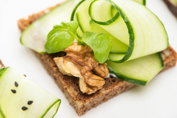 close up view of fresh cucumber toast with walnut and basil leaves isolated on white - Foto, Imagem