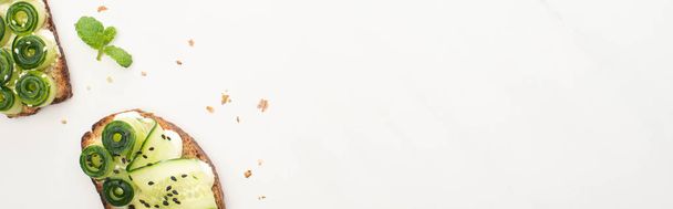 κορυφαία άποψη του φρέσκου τοστ αγγούρι με σπόρους, μέντα σε λευκό φόντο, πανοραμική λήψη - Φωτογραφία, εικόνα