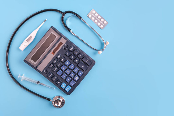 Calculatrice, seringue, thermomètre, pilules et sthétoscope sur fond bleu. coût du concept de soins de santé
 - Photo, image