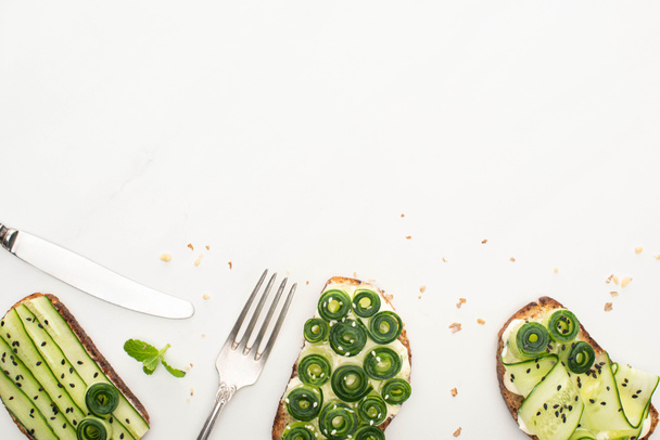 vista superior de tostadas frescas de pepino con semillas, hojas de menta y cubiertos sobre fondo blanco
 - Foto, imagen