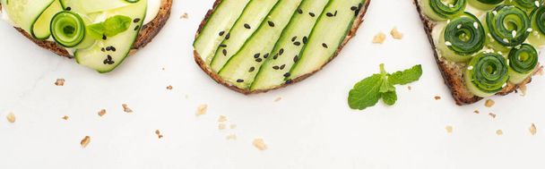 top view of fresh cucumber toasts with seeds, mint leaves on white background, panoramic shot - Fotó, kép