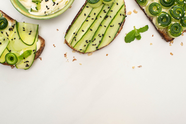 top view of fresh cucumber toasts with seeds, mint leaves near yogurt on white background - Fotoğraf, Görsel