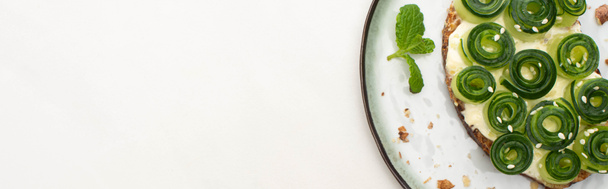 vista superior de la tostada de pepino fresco con hojas de sésamo y menta en el plato sobre fondo blanco, plano panorámico
 - Foto, Imagen