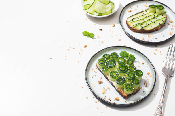 fresh cucumber toasts on plates near fork on white background - Photo, Image