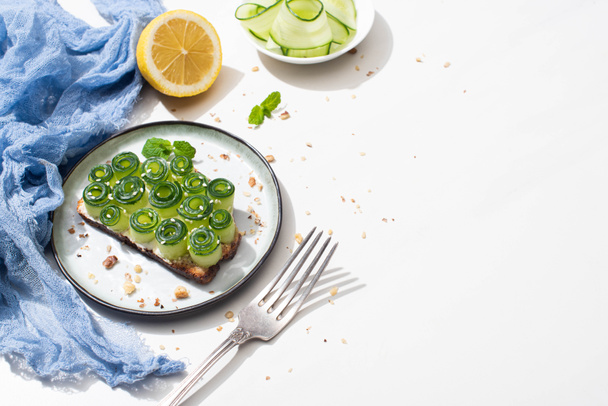 tostadas de pepino fresco con sésamo, hojas de menta cerca de tenedor y limón sobre fondo blanco
 - Foto, imagen