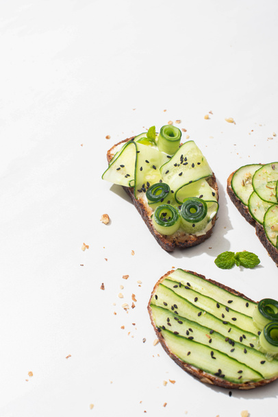 fresh cucumber toasts with seeds, mint leaves on white background - 写真・画像
