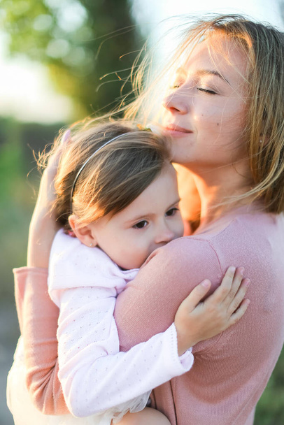 Sarışın genç anne küçük kızı kucaklıyor ve gülümsüyor.. - Fotoğraf, Görsel