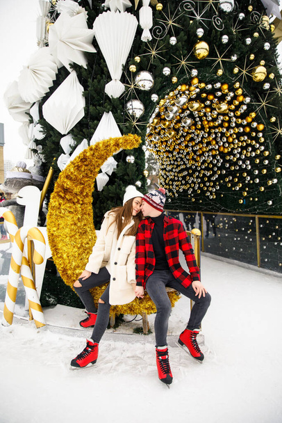 cute boy and girl in red skates kissing near Christmas tree on ice rink - Foto, Imagen