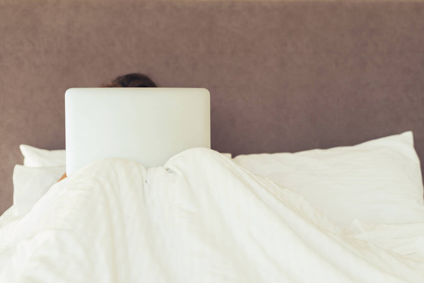 Femme avec ordinateur portable couché dans le lit et couvert de couverture
.   - Photo, image