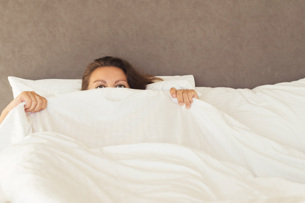 Eine junge Frau mit riesigen verängstigten offenen Augen liegt im Bett und deckt sich mit Laken und Verstecken zu. Albträume, Schlaflosigkeit, Phobien, Panikattacken. Konzept - Foto, Bild