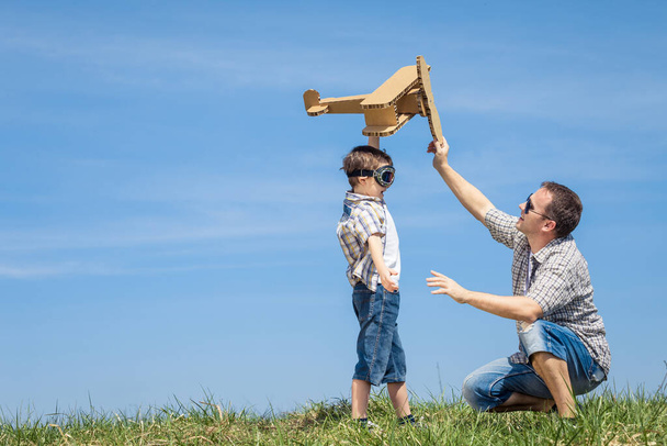 Father and son playing with cardboard toy airplane in the park at the day time. Concept of friendly family. People having fun outdoors. Picture made on the background of blue sky. - Foto, Imagen