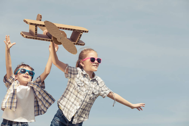 Two little kids playing with cardboard toy airplane in the park at the day time. Concept of happy game. Child having fun outdoors. Picture made on the background of blue sky. - Фото, зображення