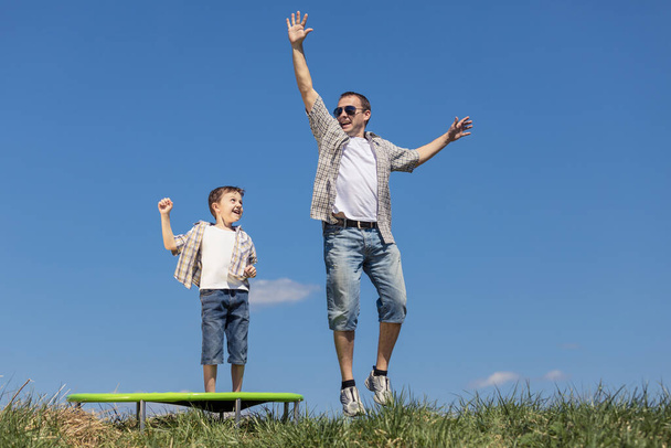 Vader en zoon spelen overdag op het veld. Mensen hebben plezier buiten. Ze springen op trampoline op het gazon. Begrip "vriendelijk gezin". - Foto, afbeelding