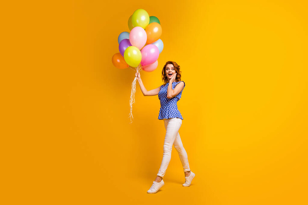 Full length photo of funny crazy lady hold many colorful balloons walk moving party birthday event wear polka-dot blue shirt white pants shoes isolated yellow color background - Foto, Bild