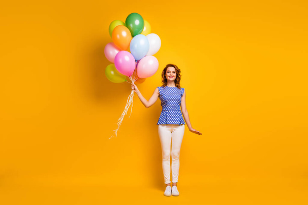 Full length photo of beautiful lady hold many colorful air balloons visit corporate event wear polka-dot blue shirt white pants gumshoes isolated yellow color background - Zdjęcie, obraz