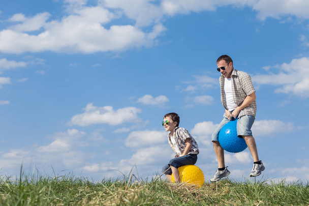 Baba ve oğul gündüz vakti sahada oynuyorlar. İnsanlar dışarıda eğleniyor. Bahçede şişme topların üzerinde zıplıyorlar. Arkadaş canlısı aile kavramı. - Fotoğraf, Görsel
