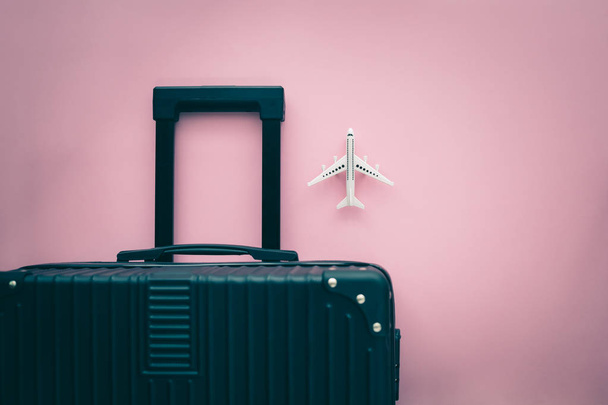Black luggage and white airplane model on pink background for travel and journey concept - Foto, Imagem