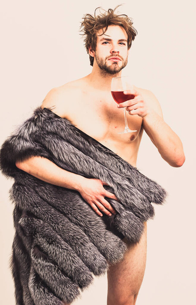 Rich athlete enjoy his life. Richness and luxury concept. Sexy sleepy rich macho tousled hair drink wine isolated on white. Guy attractive rich posing fur coat on naked body. Fashion and pathos - Photo, image