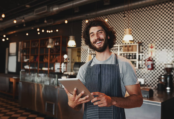 Handsome young caucasian coffee shop owner wearing apron laughing using digital tablet - Foto, Bild