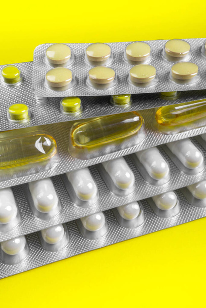 Καψάκια και χάπια συσκευασμένα σε κυψέλες σε κίτρινο φόντο. Δισκία. Σύμβολο ιατρικής. Φάρμακα - Φωτογραφία, εικόνα