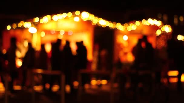 Artistieke presentatie van mensen op een markt in de avond, nacht. Sterke achterlichten achter. Winkelen. Lopen. Silhouetten, schaduwen. Verhuizen. - Video