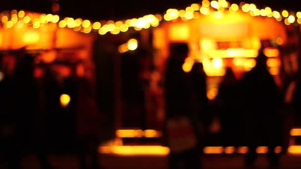 Artistieke presentatie van mensen op een markt in de avond, nacht. Sterke achterlichten achter. Winkelen. Lopen. Silhouetten, schaduwen. Verhuizen. - Video
