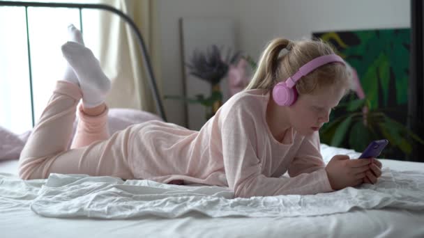 vida moderna da geração Z. adolescente em pijama e fones de ouvido no quarto na cama escuta música de um smartphone
. - Filmagem, Vídeo