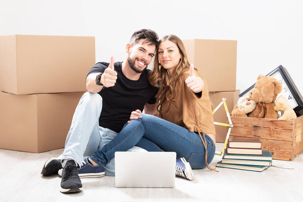 Retrato de um casal feliz Desempacotando Caixas em Nova Casa e sentado na flor
 - Foto, Imagem