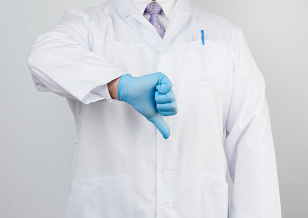 médico en un abrigo blanco con botones muestra un gesto de aversión con la mano, usando guante médico azul, emoción de negatividad
 - Foto, Imagen